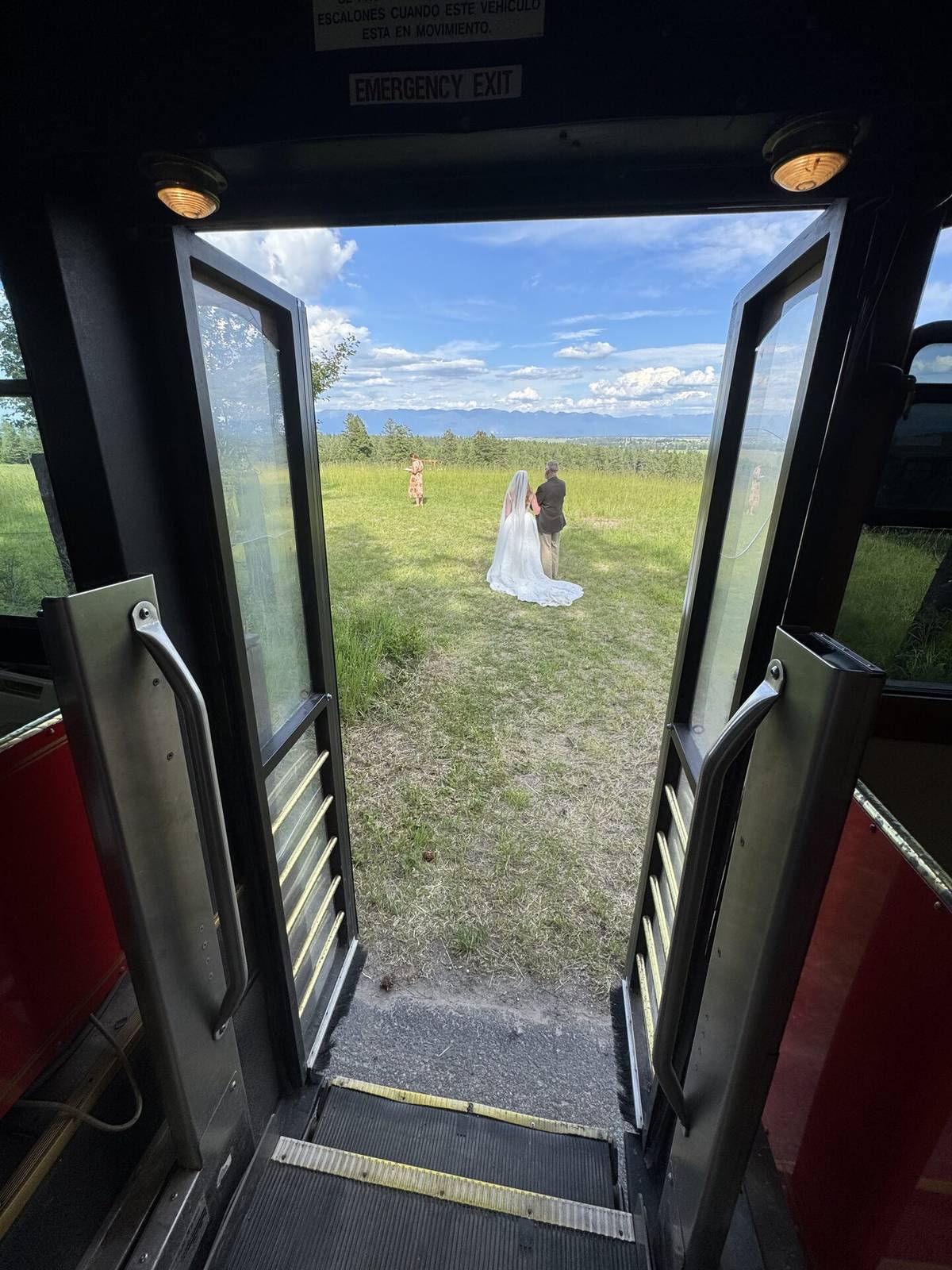 View from inside a Montana trolley looking out to a wedding couple in a mountain meadow
